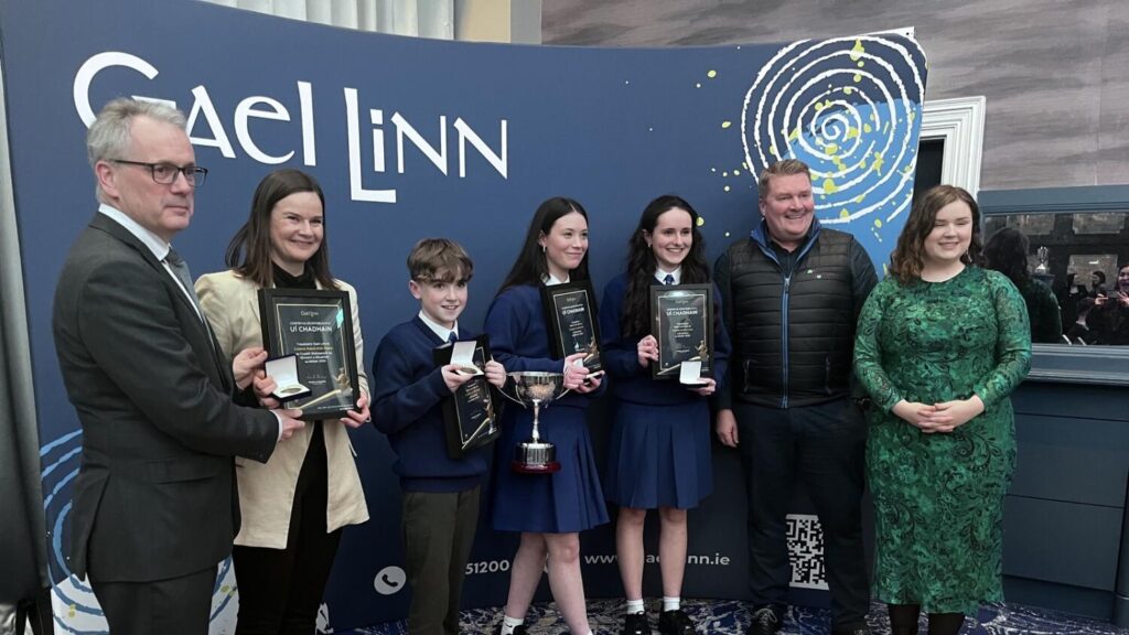 Group from Rathcairn celebrates Gael Linn award win, holding plaques and medals.