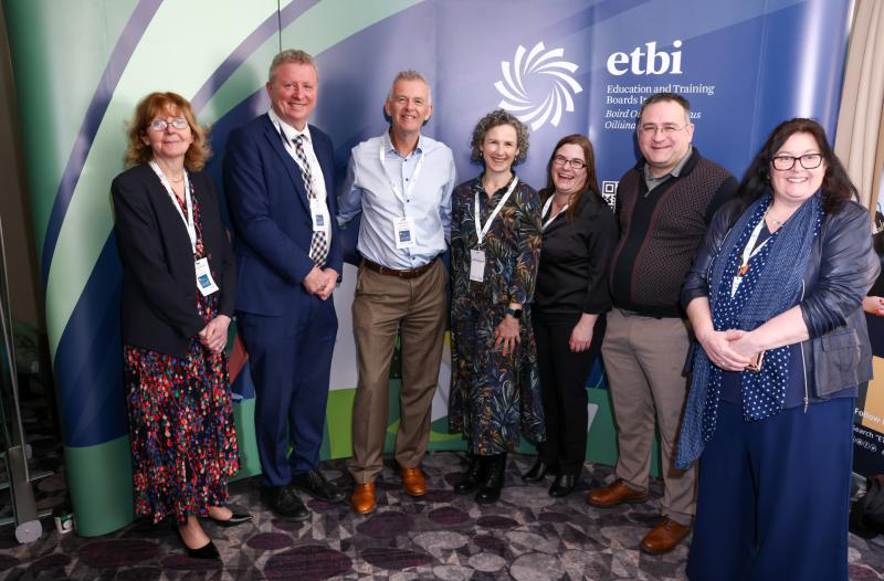 Seven participants stand smiling together at an ETBI event with conference badges.