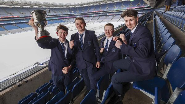 Four students in school uniforms celebrate in stadium seats, holding a trophy aloft.