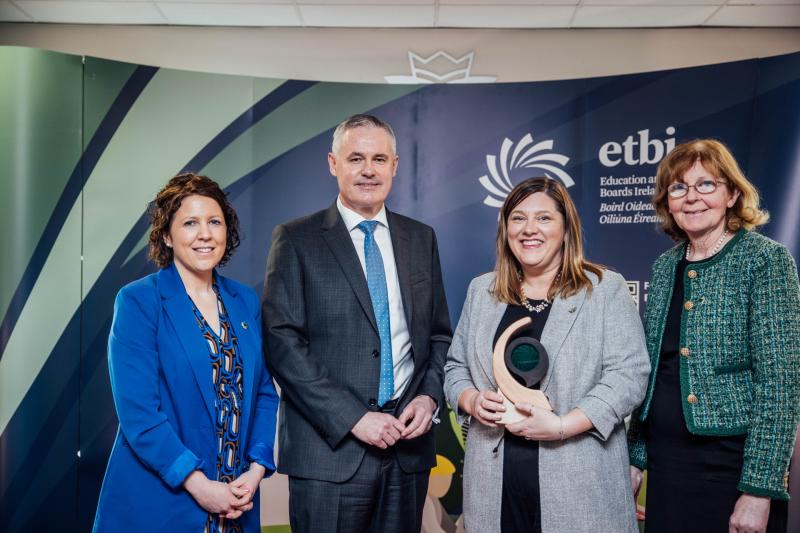 Four people stand together at an ETBI event, one holding an award for learner achievement.